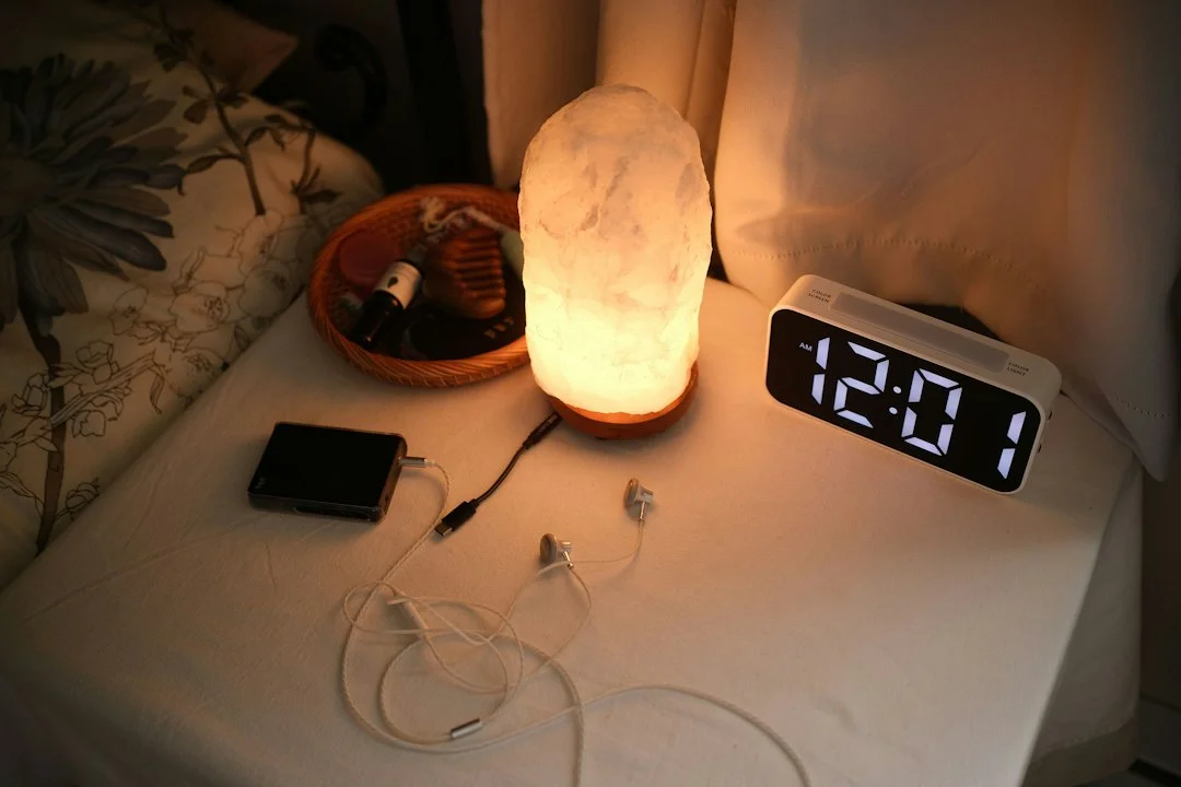 Nachttisch mit Lampe, Wecker und Ladekabeln in einem Schlafzimmer am Abend