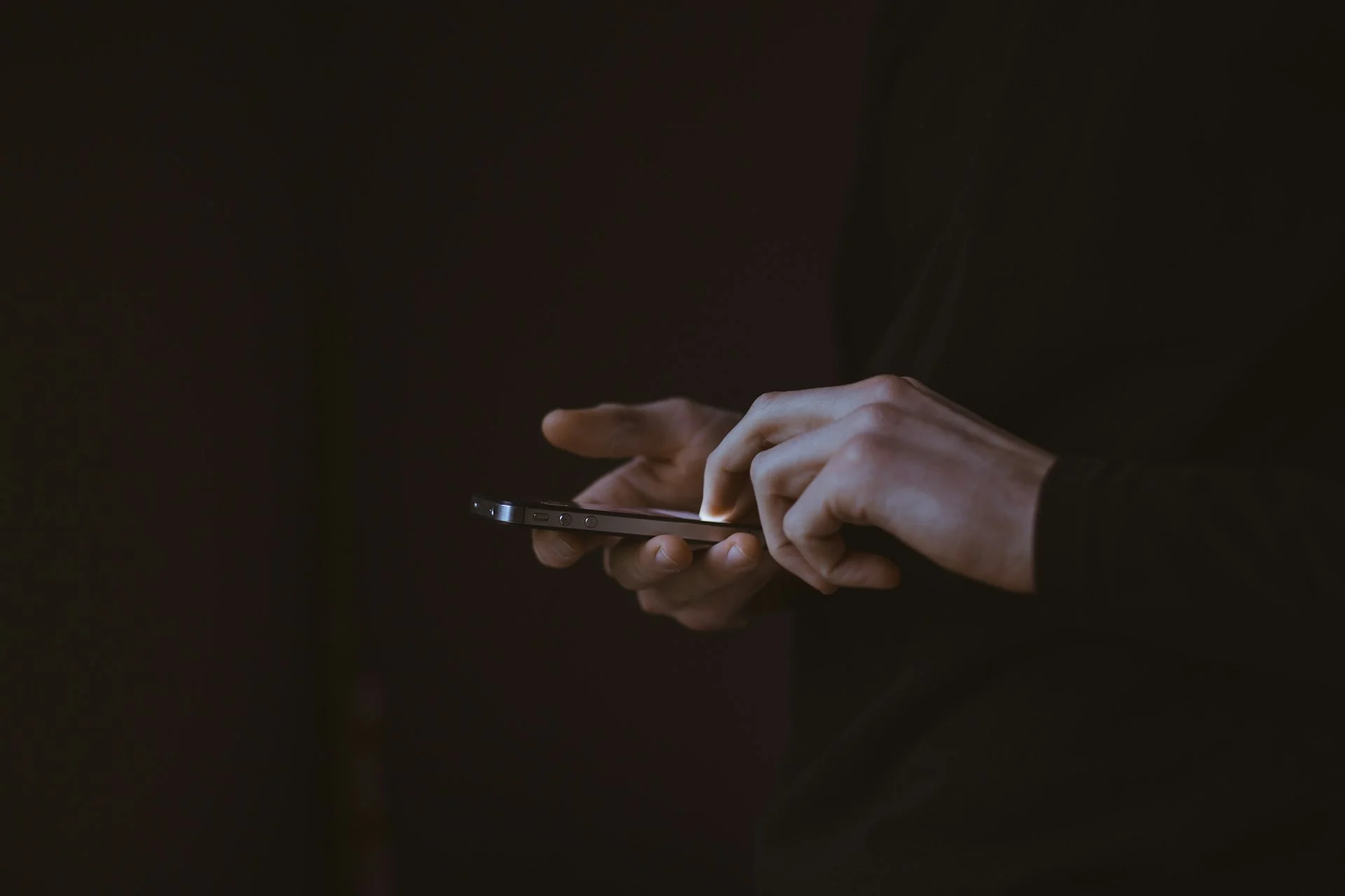 Eine Hand hält ein Handy mit beleuchtetem Display in einem abgedunkelten Raum