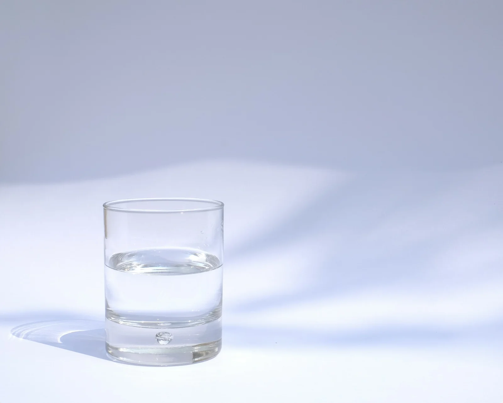 Verre d'eau posé sur une table en bois près d'une fenêtre lumineuse